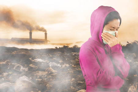 女人穿着粉红色的冬季服装，戴着口罩，在空气污染的背景下，她的鼻子上有一个寒冷和流感的健康概念。