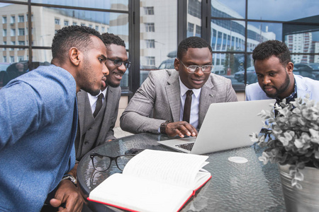 一群快乐的多样化男女商人团队在玻璃建筑的背景下, 正式聚集在明亮的办公室里, 围绕着笔记本电脑