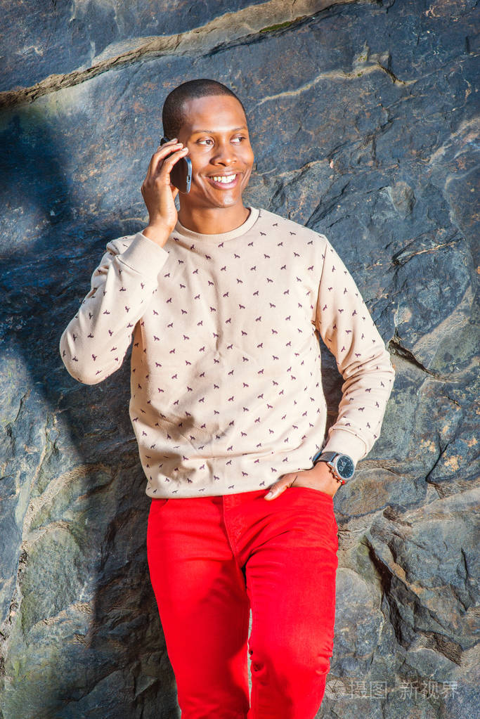 穿着奶油,图案,无领毛衣,红色裤子,戴着手表,一个年轻的黑人站在岩石