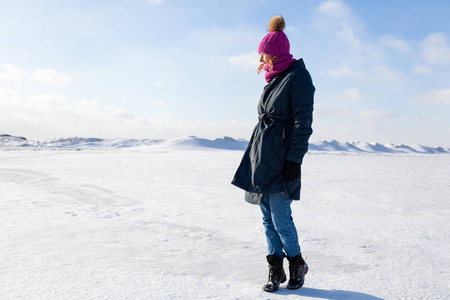 一个年轻的女人戴着粉红色的针织帽子，黑色的外套享受冬天的自然，在冬天寒冷的日子里，在北极的冰冻的海洋上绕着蓝天散步。冬季生活和户