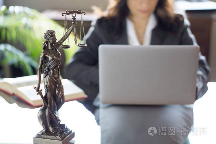 律师办公室。带有秤和在笔记本电脑上工作的律师的正义雕像