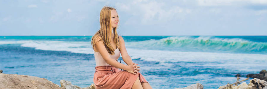 年轻的女人坐在令人惊叹的梅拉斯蒂海滩与绿松石水巴厘岛印度尼西亚。