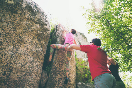 在大自然中攀爬。 朋友们爬到石头上。 女孩爬上石头，朋友们支持她。 在大自然中巨石。 积极的生活方式。 体育界人士。 体操保险。
