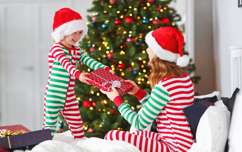 幸福的家庭母亲抱着她的小儿子穿着睡衣，在圣诞节早上圣诞节前夕打开礼物