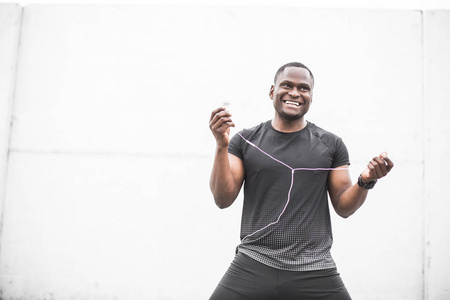 微笑年轻的男性慢跑运动员训练和做户外锻炼在城市。一个黑人在锻炼后休息, 听音乐, 看体育手表。文本的可用复制空间
