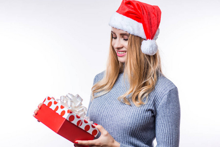 快乐漂亮的年轻女人拿着礼品盒在白色背景上。 穿着灰色毛衣和红色圣诞帽的漂亮女孩