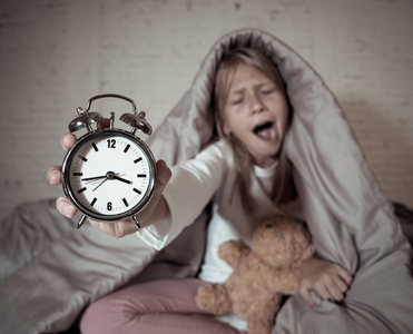 可爱的失眠小女孩坐在床上,闹钟看起来很累,有睡眠问题,晚上睡觉,或者