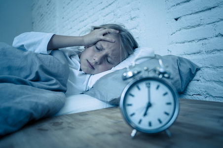 夜醒甜蜜的失眠小女孩躺在床上悲伤地看着闹钟,不得不醒来,但在烦恼中