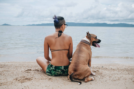 快活的，漂亮的年轻女人在海滩上坐着拥抱她的狗