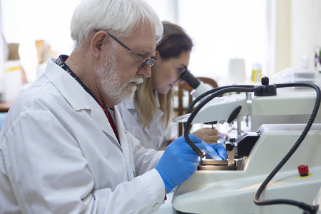 保健研究人员在生命科学实验室工作。 年轻的女性研究科学家和高级男性主管在研究实验室准备和分析显微镜幻灯片。