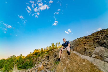 带背包的男性徒步旅行者在巨大的岩石边缘放松。 游客从岩石上欣赏到美丽的景色。