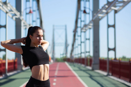 有吸引力的健身女人在桥上慢跑之前做手伸展运动。 空的空间