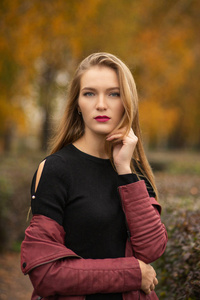 可爱的金发女人，红唇，穿着毛衣和夹克，在秋天公园摆姿势