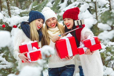 一群年轻女孩在户外用圣诞礼物自拍。 快乐的朋友在手机上拍照