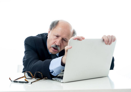 愤怒和疲惫的成熟商人在办公桌上过度劳累，不理解老年人对笔记本电脑的感知和使用，加班压力和过度工作的概念孤立在白色背景下。