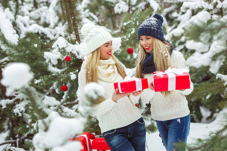 女朋友在户外玩圣诞礼物。 女人拿着礼物。 女士们在冬天的背景下拿着红色的盒子
