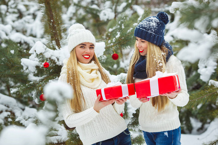 女朋友在户外玩圣诞礼物。 女人拿着礼物。 女士们在冬天的背景下拿着红色的盒子