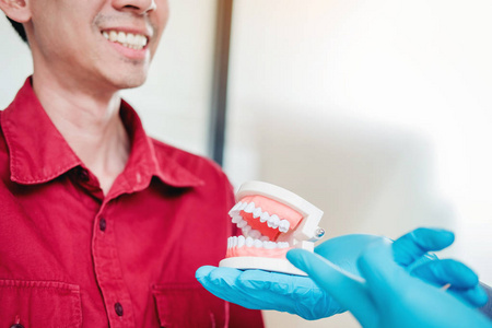 牙科医生与微笑的男性病人交谈，并在牙科室出示假牙