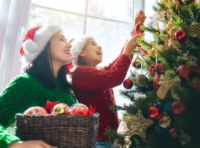 圣诞快乐，节日快乐 妈妈和女儿在室内装饰圣诞树。 圣诞节前的早晨。 肖像爱的家庭亲密。