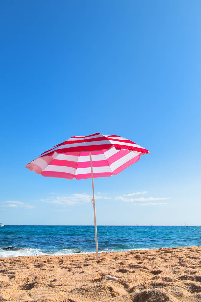空旷的海滩，有海浪大海和条纹的粉红色阳伞