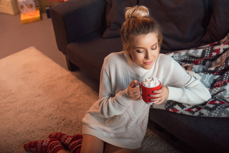 美丽的女人坐在圣诞图案的袜子地毯上，上面有可可杯