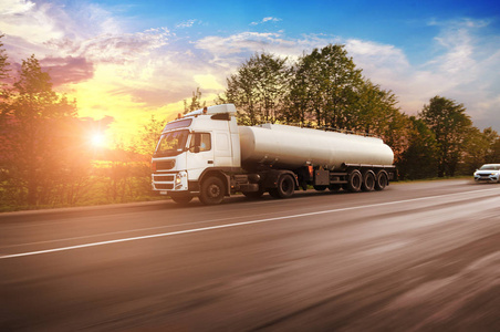 大型金属燃料油罐车运输燃料在乡村道路上运动，树木与天空，日落