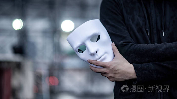 黑色夹克男手拿着白色面具. 匿名社会掩蔽或主要抑郁障碍概念.