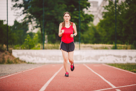 胸部大,穿着红色t恤和短裤,在一个有红色橡胶涂层的体育场跑步