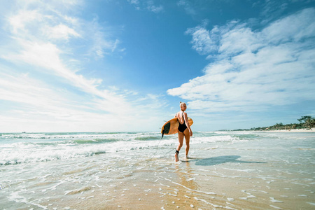 美丽的和运动的女孩冲浪者走与董事会在海滩上的日出。积极的生活方式和娱乐
