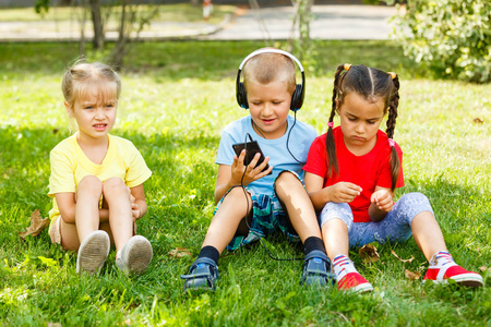 公园里带着智能手机坐在草地上的孩子们的陪伴