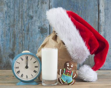 木制桌子背景上的一杯牛奶美味的巧克力饼干和圣诞老人帽子