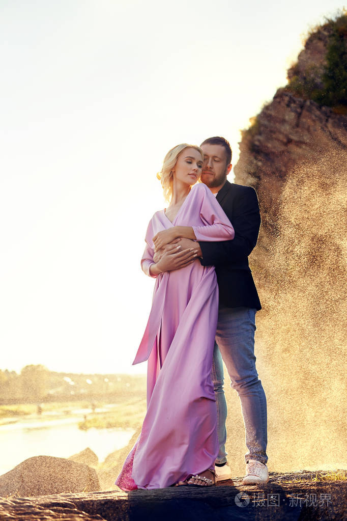 男人和女人在夏天日落时穿着漂亮的衣服拥抱一对相爱的夫妇站在岸边的