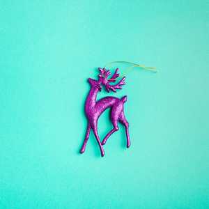 绿松石背景上闪闪发光的紫鹿圣诞节玩具。 极简主义。