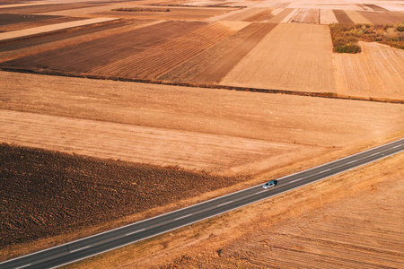 鸟瞰汽车驾驶在道路上通过平原农村在阳光明媚的秋天下午从无人机POV。