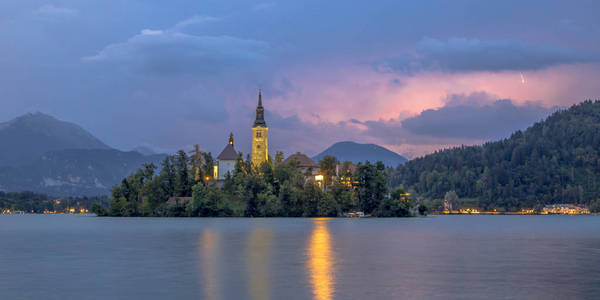 s church and mountains in backdrop under stormy sky with lightni