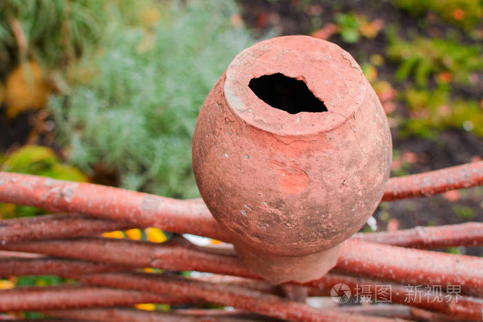 一个破碎的棕色陶罐倒挂在木头栅栏上