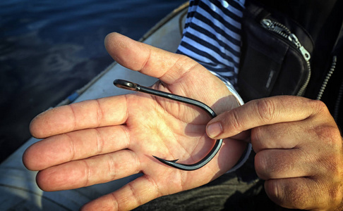 大钩以渔夫手掌为背景的大型鱼钩照片