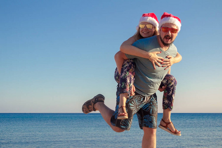 英俊的嬉皮士男子给小猪回来给他的女朋友在海边的圣诞帽子和眼镜