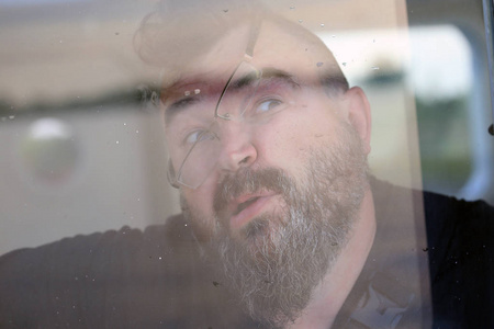 戴着眼镜的悲伤成年男性的特写肖像将他的脸贴在玻璃上照片