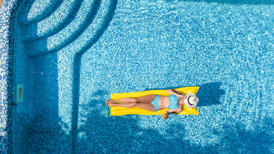 美丽的年轻女孩在游泳池里放松，在充气床垫上游泳，在家庭度假热带假日度假胜地的水中享受乐趣，从上面可以看到空中无人机。
