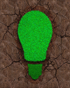 绿草在干燥的红壤上以灯泡的形式出现，具有裂缝背景的生态和可再生能源概念。