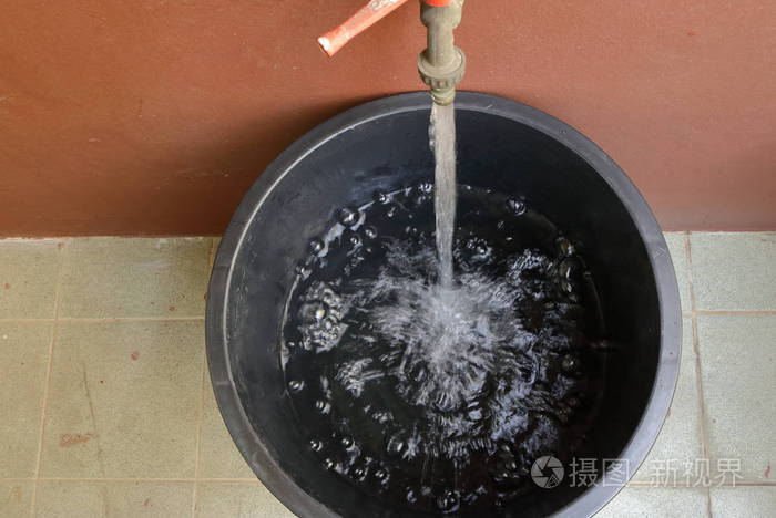 在肮脏的地板上水流入一个大黑桶的顶部视图节约概念