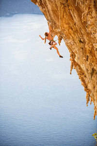 穿比基尼的年轻女性攀岩者，一只手悬在悬崖上
