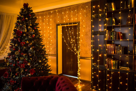 圣诞树假日家庭内部灯光花环，以及家庭装饰品。新年的风景细节。红色浆果，圣诞灯，黑暗的房间，红色和金色的球。