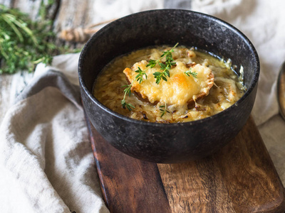 传统的法国洋葱汤，配土司奶酪和新鲜的百里香，放在黑碗里，放在木棕色的木板上