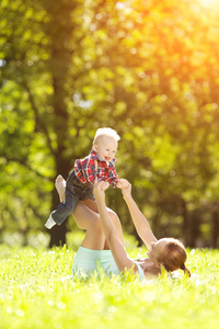 可爱的小宝宝在夏天的公园里和妈妈在草地上。 可爱的宝贝和妈妈在户外。 微笑的情感孩子和妈妈散步。 微笑的微笑