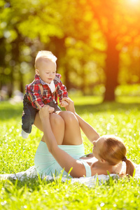 可爱的小宝宝在夏天的公园里和妈妈在草地上。 可爱的宝贝和妈妈在户外。 微笑的情感孩子和妈妈散步。 孩子的微笑