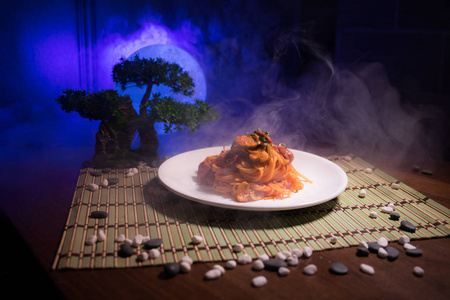 关闭盘子的视图与日本食物在里面。 日本传统食品在木桌上装饰盆景，树和月亮在色调雾背景。