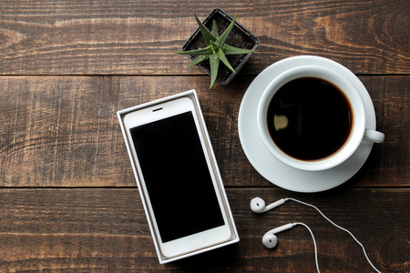 带耳机的智能手机和棕色木桌上有咖啡的杯子。 上文视