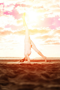 年轻漂亮的苗条女人在日落时在海滩上练习瑜伽。 日出时瑜伽